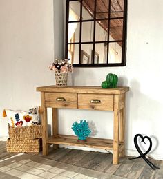 a wooden table with two drawers and a mirror on the wall above it next to a basket