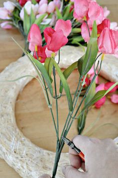 a person cutting flowers with scissors on a wooden table in front of some wreaths