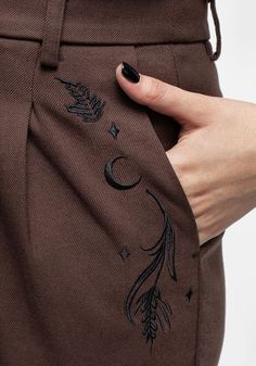 a woman's hand is holding onto the pocket of her brown pants with an embroidered design on it