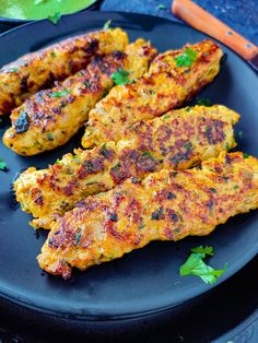 two pieces of chicken on a black plate with carrots and parsley in the background