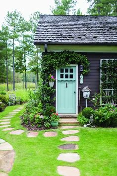 a small house with a green door surrounded by greenery and stepping stone walkways