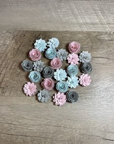 small paper flowers are arranged on a wooden surface, in pastel pink and grey colors