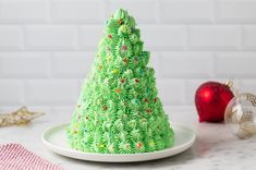 a green christmas tree cake sitting on top of a white plate next to an ornament