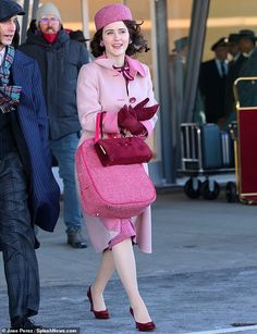 a woman in a pink coat and hat is walking down the street with her handbag