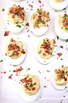 deviled eggs topped with bacon and chives on a white platter, ready to be eaten