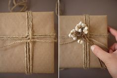 a hand holding a wrapped present box with twine and pearls on the top, while another person holds it in their left hand