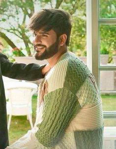 two men standing next to each other in front of a window with the same sweater on