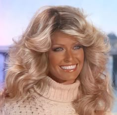 a woman with long blonde hair smiling at the camera while wearing a turtle neck sweater