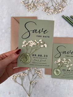 save the date cards with white flowers and wax stamp on them are being held by a woman's hand