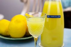 a glass filled with yellow liquid next to lemons on a blue tablecloth and plate