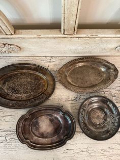 four metal plates sitting on top of a white wooden table next to an old door