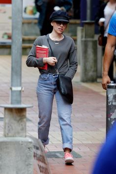 a woman walking down the street with a book in her hand and a hat on