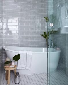 a white bath tub sitting next to a wooden stool in a bathroom under a window