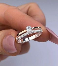 a woman's hand holding a ring with two diamonds on it and the middle finger