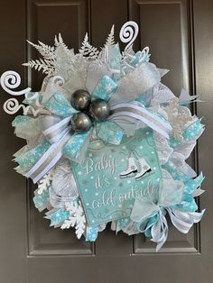 a blue and white christmas wreath with silver bells on the front door that says, baby it's cold outside