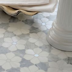 a white vase sitting on top of a marble floor next to a table with a cloth draped over it