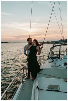 a man and woman standing on the bow of a sailboat in the ocean at sunset