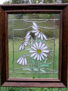 a stained glass window with white daisies in the center and green grass behind it