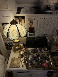 a white table topped with lots of clutter next to a lamp and pictures on the wall