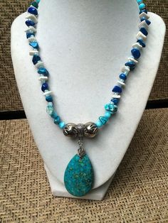 "This vibrant gemstone and sea shell necklace set is handmadeartfully arranging turquoise Howlite gemstones with blue rock quartz, blue glass beads, pieces of white seashell, silver Rhodium accent beads and small silvertone metal beads.  It is further enhanced with a turquoise stone  pendant which measures an inch and a half (4cm) wide and 2\" (5cm) long.   The necklace measures 18\" (46cm)  long excluding the pendant, and is finished with a decorative silver ring clasp. The matching bracelet st Bohemian Turquoise Howlite Necklace, Healing Howlite Turquoise Jewelry, Healing Turquoise Howlite Jewelry, Blue Beaded Dangle Necklaces With Natural Stones, Blue Beaded Necklaces With Natural Stones And Dangle Shape, Blue Beaded Necklaces With Natural Stones, Blue Turquoise Teardrop Necklace With Gemstone Beads, Artisan Turquoise Necklace With Natural Stones For Beach, Bohemian Howlite Jewelry With Natural Stones