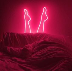 a bed with a red comforter and two neon lights in the shape of women's legs