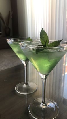 two martini glasses with green liquid and a mint sprig on the rims