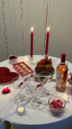 a table topped with wine glasses and plates filled with food next to two red candles