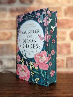 the book daughter of the moon goddess is sitting on a wooden table next to a brick wall