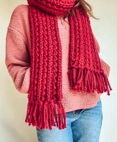 a woman wearing a red knitted scarf with tassels on the ends, standing in front of a white wall