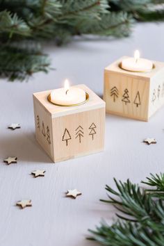 two wooden blocks with candles on them sitting next to evergreen branches and pine cones in the background