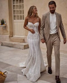 a man and woman are walking down the street holding hands while dressed in wedding attire