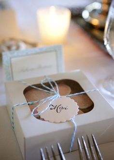 a white box with a tag tied to it sitting on top of a table next to silverware