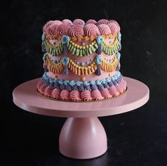 a multi - layered cake with colorful icing on a pink plate, against a black background