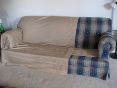 a couch that has been covered with a blanket and is sitting on the floor next to a lamp