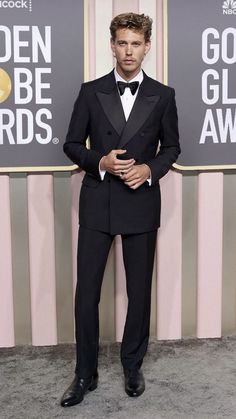 a man in a tuxedo and bow tie standing next to a pink wall