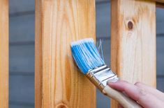 a person holding a paintbrush in their hand near a wooden fence with wood slats