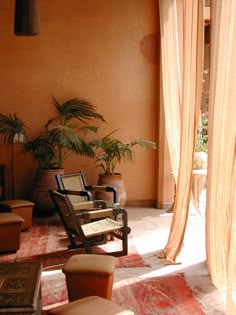 an outdoor area with chairs and potted plants on the floor, in front of a large orange wall