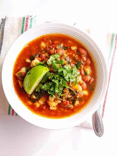 a white bowl filled with chili and beans on top of a striped towel next to a spoon