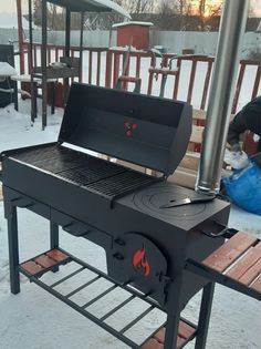 a bbq grill sitting on top of a wooden table covered in snow next to a blue bag