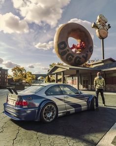 a man standing next to a car in front of a doughnut shop with a giant donut on top