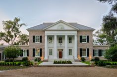 a large white house with black shutters on the front and side windows, surrounded by greenery