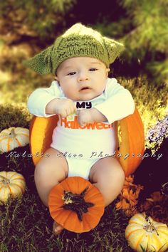 a baby sitting in the grass wearing a hat and holding an orange pumpkin with his hands