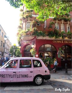 a small pink car parked in front of a building with flowers growing on it's roof