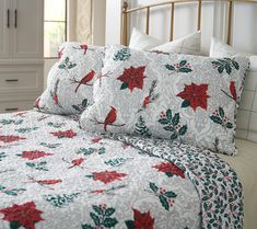 a white bed with red and green poinsettis on the sheets, pillows and pillow cases