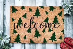 a welcome mat with trees on it next to red shoes and succulents