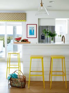 two yellow stools sitting in front of a kitchen counter with a basket on the floor