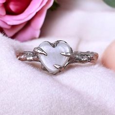 a heart shaped ring sitting on top of a white blanket next to a pink rose