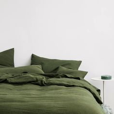 a bed with green sheets and pillows in a white room next to a small table