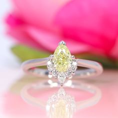 a yellow diamond ring sitting on top of a white surface next to a pink flower