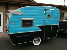 an old blue and black trailer parked in front of a building next to a car